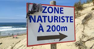 Panneau en bord de plage indiquant « Zone naturiste à 200 m », avec une flèche vers la droite.