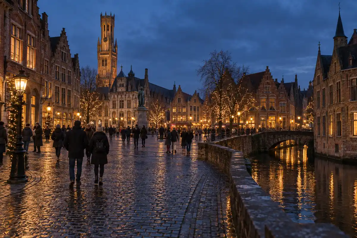 Vue large de Bruges au crépuscule, avec des visiteurs sur des pavés mouillés, des arbres illuminés, des façades flamandes historiques et un canal reflétant les lumières.